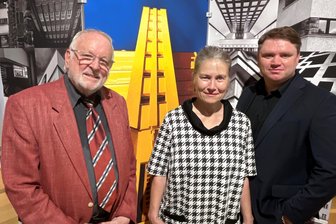 Von der Textilfachschule bis zum Wasserturm: Wie ein Baustil eine Vogtland-Stadt prägt - Wolfgang Viebahn, Martina Bundszus und Carsten Steps (v. li.) vor einer Fotowand mit Bauten.