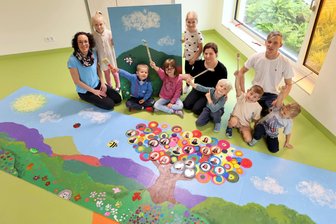 Von Kindern für Kinder: Zwickauer Kita „Marienhof“ bekommt Wandbild - Kita-Leiterin Jessica Clauß (links), Künstlerin Manuela König und der stellvertretende Kitaleiter Tobias Fröhlich zeigen zusammen mit Kindern das Kunstwerk.