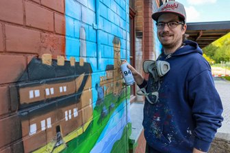 Vor Landesgartenschau: Alter Bahnhof im Erzgebirge bekommt bunte Fassade - Der Graffiti-Künstler Robert Lemcke hat damit begonnen, die Fassade des Bahnhofs Niederschlema auf der Seite zum Bahnsteig hin zu besprühen.