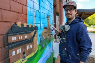 Vor Landesgartenschau: Alter Bahnhof im Erzgebirge bekommt bunte Fassade - Der Graffiti-Künstler Robert Lemcke hat damit begonnen, die Fassade des Bahnhofs Niederschlema auf der Seite zum Bahnsteig hin zu besprühen.
