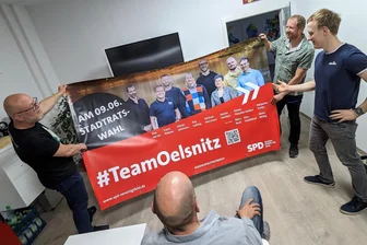 Wahlkampfpläne bei Partypizza und Bier: Warum die Oelsnitzer SPD vor der Stadtratswahl optimistisch ist - Sören Wittig (v. l.), Stefan Fleischer-Seifert, Kay Ludwig und Benjamin Trinks sind vor dem Endspurt im Wahlkampf mit dem neu eingetroffenen Plakat zufrieden. Sie treten für die Liste der SPD an – und sind guter Dinge für den 9. Juni.