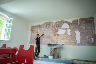 Wandgemälde: Wer soll das bezahlen? - Friedhofsmitarbeiter Thomas Bruder vor den bislang freigelegten Resten des historischen Wandbildes in der Augustusburger Kapelle.