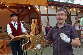Wartehalle der Rentzschmühle wieder aufgebaut: Gockescher Hahn dreht sich nun auf dem Kulturbahnhof - Marco Döbel, der großen Anteil am Wiederaufbau der Bahnwartehalle Rentschmühle hat, setzte den Gockeschen Hahn zur Krönung aufs Dach des "Kulturbahnhofs". Jörg Gemeinhardt (hinten links) blickte auf den gesamten Prozess von der Idee bis zur Umsetzung des Projekts zurück.