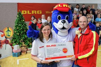 Warum Lebensretter eine Glauchauer Schule auszeichnen - Lehrerin Anja Haberkorn und DLRG-Landespräsident Andreas Lorenczat freuen sich mit Maskottchen Nobbi über den Förderpreis.