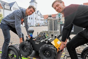 Warum Roboter Husky die Innenstadt von Freiberg erkundet - Erster Ausflug für den Husky: Die wissenschaftlichen Mitarbeiter an der TU Bergakademie Freiberg, Norman Seyffer (l.) und Lorenzo Neumann, heben den Testroboter auf den Obermarkt.