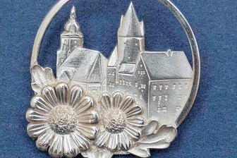 Warum Schwarzenberg 2022 erneut keine Ehrennadeln verleiht - Die silberne Ehrennadel "Schwarzenberger Edelweiß". Sie zeigt Schloss und Kirche als Wahrzeichen der Stadt, dazu zwei Blüten der als Schwarzenberger Edelweiß bekannten Spanischen Wucherblume - das Ganze in einem Ring, der symbolisch für die Perle des Erzgebirges steht, wie sich Schwarzenberg gern nennt.