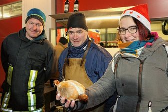 Was es mit der neuen Feuerwehr-Wurst im Vogtland auf sich hat - Michael Wermig (links) und Tanja Weber von der Feuerwehr sowie Janko Wohlleben von der gleichnamigen Fleischerei in Pausa zeigen die erste fertige Pausaer Feuerwehr-Wurst mit Tzatziki und Krautsalat im speziellen Brötchen.