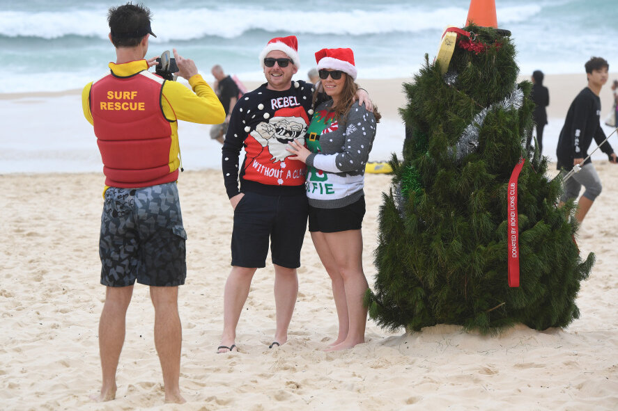 Was Sie so noch nicht über Weihnachten wussten - Ein Pärchen am australischen Strand Bondi Beach lässt sich von einem Rettungsschwimmer neben einem Weihnachtsbaum fotografieren.