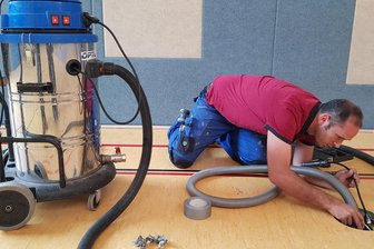 Wasserschaden in Oelsnitzer Sporthalle: Was im schlimmsten Fall droht - Ein Mitarbeiter der Firma Morgner versucht, das Wasser unter dem Sportboden abzusaugen.
