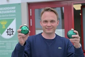 Weihnachtsatmosphäre mitten im Sommer: Dorf im Erzgebirge „schiebt“ Schwibbogen an - Niederdorfs Bürgermeister Stephan Weinrich mit zwei der Niederdorfer Christbaumkugeln. Am Wochenende wird es in der Gemeinde weihnachtlich.
