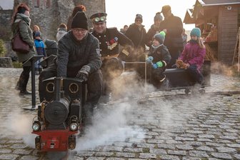 Weihnachtsmarkt wie zur Gründerzeit: Was die historische Schlossweihnacht im vogtländischen Oelsnitz so besonders macht - Nico Seidl begeisterte als Lokführer die Besucher zur historischen Schlossweihnacht auf Schloss Voigtsberg in Oelsnitz mit seiner fahrbaren Dampfeisenbahn. Auch Markus Preller aus Morgenröthe-Rautenkranz und seine Kinder hatten ihre Freude dabei.