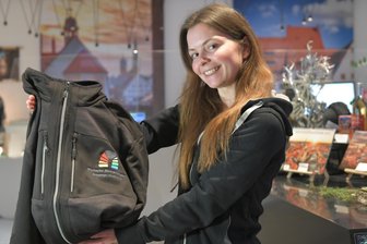 Welterbe-Jacke gibt es auch in Freiberg – wird sie Kult? - In der Touristinformation Freiberg zeigt Mitarbeiterin Jasmin Faust die Jacke zum Welterbe Montanregion Erzgebirge.