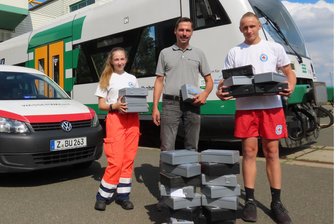Werdau: Was die Rotkreuzler mit ungenutzten Verbandskästen machen - Benjamin Drechsler (Länderbahn, Mitte) übergibt die Verbandskästen an Saphira Kurze und Karl Schwedler.