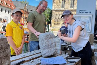 Werkstattwoche in Zwickau: Warum eine 15-Jährige den Marx-Kopf in Stein meißelt - Bildhauer Sebastian Harbort gibt Mimi Lobsa (15) Tipps bei ihrer Arbeit am Karl-Marx-Kopf. Anton Harbort (10) hört mit zu.