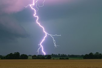 Wetterdienst warnt im Erzgebirge kurzzeitig vor schwerem Gewitter - Ein Blitz leuchtet über einer Landschaft auf. Für Freitagabend warnt der Deutsche Wetterdienst vor schweren Gewittern im Erzgebirge.