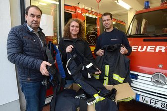 Wie die Grünbacher Feuerwehr und eine Ellefelder Spedition die nächste Fahrt des Hilfsvereins Keimling nach Rumänien unterstützen - Bürgermeister Ralf Kretzschmann (l.), Yvonne Dietz vom Verein und Michael Breitfeld von der Feuerwehr verpacken ausgemusterte Feuerwehrkleidung.