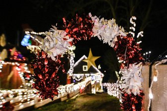 Wie ein „etwas weniger“ Weihnachten bereichern kann: Experte gibt in Freiberg Tipps - Was macht Weihnachten aus? - Geschmäcker sind verschieden: Überdimensionale Zuckerstange aus rot-weißem Lametta an einem Zaun vor dem weihnachtlich geschmückten Haus.