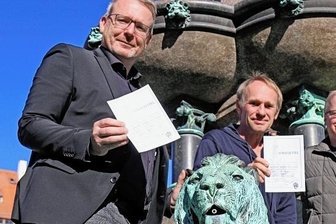 Wie "Keimzeit" für ihr Tivoli-Konzert werben - Freibergs OB Sven Krüger verpasst Keimzeit-Frontmann Norbert Leisegang und Kai Suttner, künstlerischer Leiter des Tivoli (von links) "Strafzettel" für den verbotenen Ritt auf dem Löwen des Otto-Brunnens.