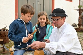 Wie macht man eine Sense wieder scharf? Kinder auf der Rochsburg haben es erfahren - Fritz und Luise dengelten beim Kinderhandwerkermarkt auf der Rochsburg bei René Lautrich eine Sense.