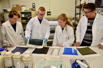 Wie viel hinter Alltagsbegleitern steckt: Schüler machen sich ihren eigenen Rucksack - Die Projektteilnehmer Yasmin Sophie Fieback (li.), Sophie Virginie Härtig und Wafa Yakdi (re.) haben unter Anleitung von Azubi Florian Gielsok Farbe auf ihre Rucksäcke aufgetragen.