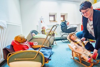 Wieso das Schatzhaus in Eibenstock große Wäsche macht - Das Schatzhaus Erzgebirge hat in einer Sonderausstellung Spielzeug aus der Zeit von 1900 bis 1989 zusammengestellt. Dazu gehören Teddys und Puppen, wie die mit dem Porzellankopf, die Leiterin Antina Richter im Puppenschlitten zurechtrückt.