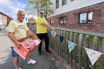 Wimpelketten, Strohfiguren und historische Drucke: So putzt sich Rotschau für die 700-Jahr-Feier heraus - Werner Barschdorf vom Ortschaftsrat (l.) und Lars Kober vom Heimatverein bringen am Gartenzaun vor der Turnhalle Wimpelketten an, die die Rotschauer selbst für die 700-Jahr-Feier des Ortes genäht haben.