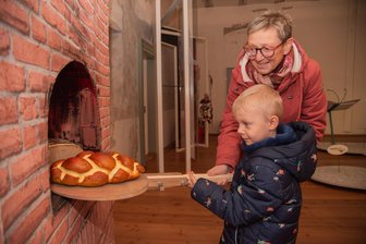 Winterausstellung in Oelsnitz: „Frau Holle“ lädt Familien auf Schloss Voigtsberg zum Mitmachen ein - Wie im Märchen Frau Holle: Simone Jahn und Enkel Marlo ziehen ein Brot aus dem Ofen.