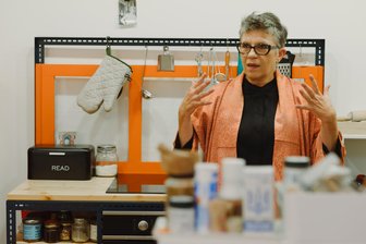 Wir gehen rein: Die Küche aus der Garage - wie die Kuratorin des Kuha-Garagenprojekts wohnt - Garagen-Kuratorin Agnieszka Kubicka-Dzieduszycka in ihrer Chemnitzer Küche, in der ein altes, orangefarben gestrichenes und auf die Seite gelegtes Fenster als Spritzschutz für den Herd dient.
