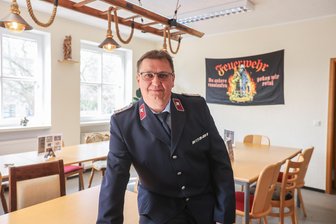 „Wo andere rauslaufen, gehen wir rein“: Die feuerwehrverrückte Familie aus Mühlau und ihre Traumata - Feuerwehrchef Jörg Voigt steht im Feuerwehrvereinszimmer, in dem sich früher das Wohnzimmer seiner Familie befand.