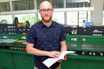 Wo per Hebel die Signale gestellt werden - Jonas Apfelbeck im Obergeschoss des elektromechanischen Stellwerks B 13 vor dem breiten Pult mit Zustimmungs-/Befehlsheben (in Grün), Fahrstraßensignalhebeln (in Rot) und Weichenhebeln (in Blau).