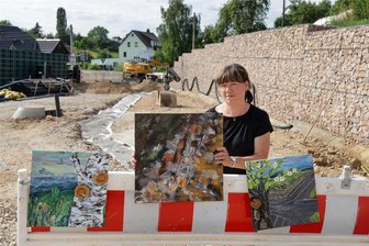 Wolfsschlucht Langenchursdorf: Megaprojekt wird zur Inspiration - Seit Beginn der Bauarbeiten in der Wolfsschlucht in Langenchursdorf hält Jana Gutte das Geschehen vor ihrer Haustür in Bildern und Drucken fest. Hier steht sie mit drei dieser Arbeiten vor einer neu errichteten Stützwand aus Steinkörben.