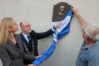Würdigung: Elsterberger Schulzentrum heißt jetzt "Wolfram Markert" - Die Leiterin des Trias-Gymnasiums und der Mittelschule, Cornelia Kiesewetter, Bürgermeister Sandro Bauroth (FDP) und Grundschulleiter Thomas Müller (rechts) enthüllten am Montagabend die Ehrentafel an der Fassade des Elsterberger Schulzentrums, das jetzt Wolfram Markert heißt. 
