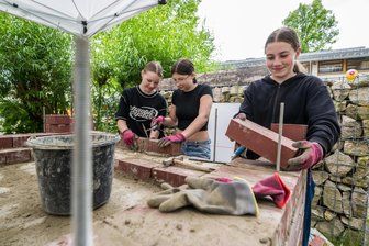 Ziegel für Ziegel zum eigenen Pizza-Ofen: Warum Schüler in Eibenstock Mörtel anrühren und mauern lernen - Elena Unger, Hanna Hahn und Judith Unger (v. l.) setzen die Ziegelsteine für den Pizza-Ofen, der bei der Oberschule Eibenstock entsteht.