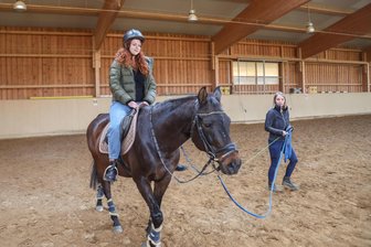 Zum ersten Mal reiten als Erwachsene: Was ist das für ein Gefühl? - Oleksandra Patlai reitet zum ersten Mal in ihrem Leben. Reitlehrerin Alexandra Dutsch führt „Karthago“ durch die Reithalle.