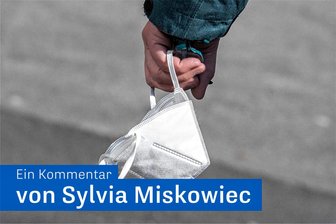 Zurück zur Maske – aber freiwillig! - Eine Passantin trägt in einer Fußgängerzone ihre FFP-2 Maske am Handgelenk.